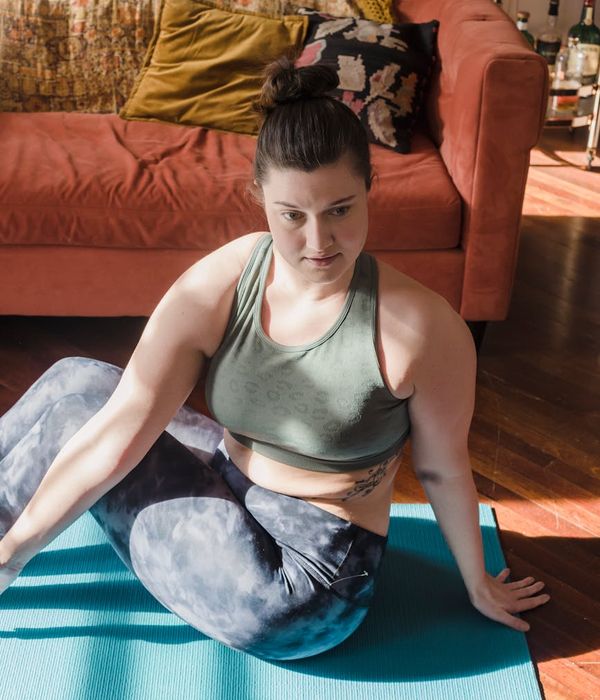 Woman performing a gentle yoga stretch in a dark room with teal light.